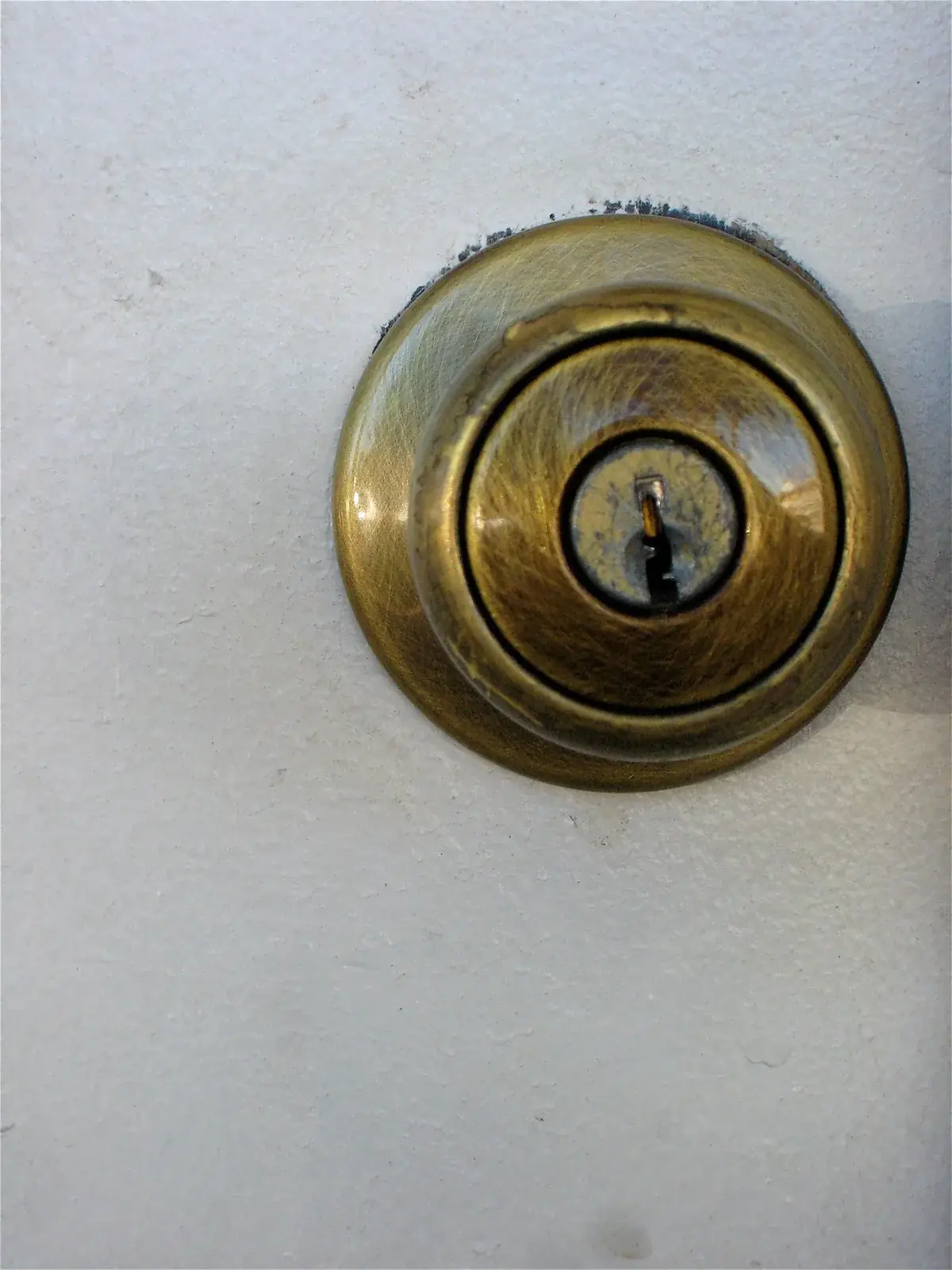 close-up of a worn brass deadbolt lock with its keyhole on a white door