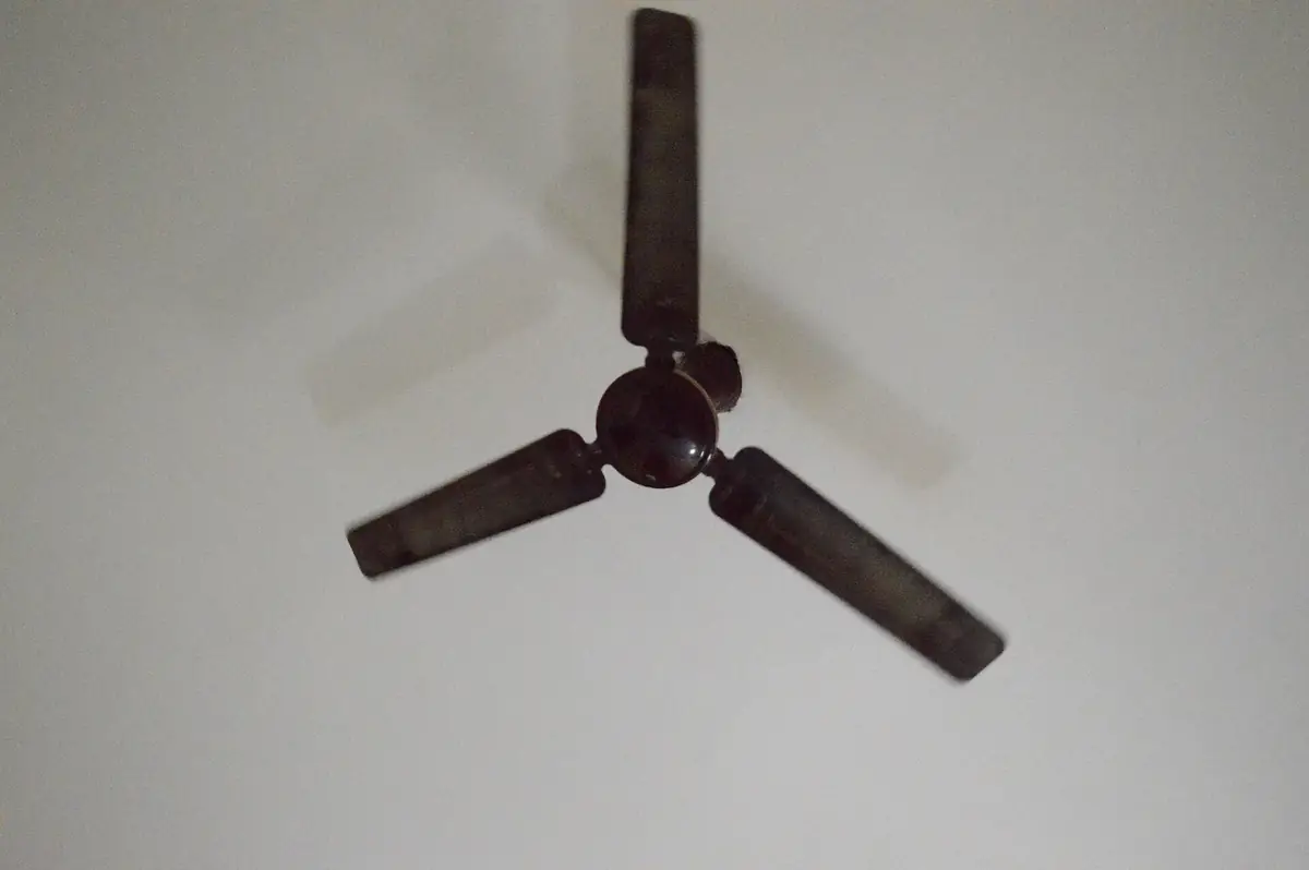 a three-blade ceiling fan with dark blades turning against a plain white ceiling