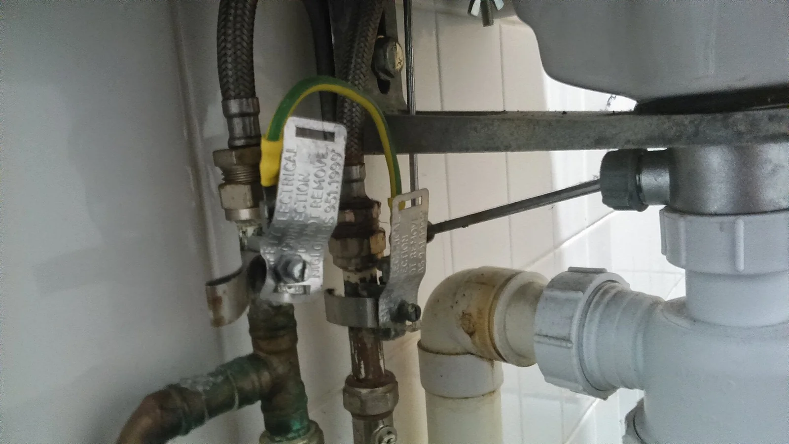 the plumbing under a sink: braided supply hoses, shutoff valves, copper pipes and a white plastic drain trap
