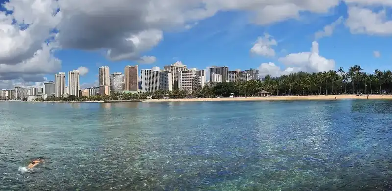 waikiki's row of high-rise hotels behind the beach, seen across clear shallow water with a swimmer