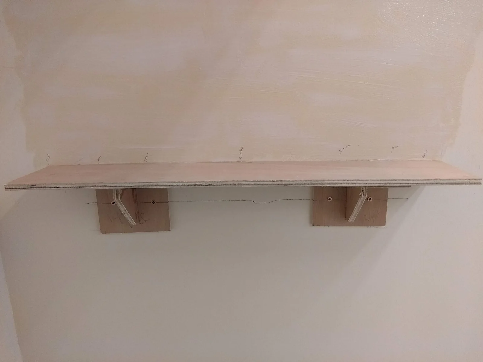 a plain wooden shelf mounted on a light wall with two wooden brackets