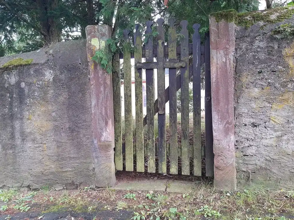 a weathered wooden picket gate set between stone posts in an old mossy wall