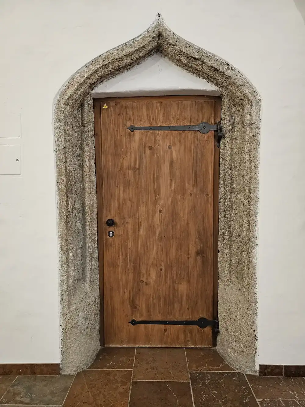 a wooden plank door with two black strap hinges set in a stone door frame in a white wall